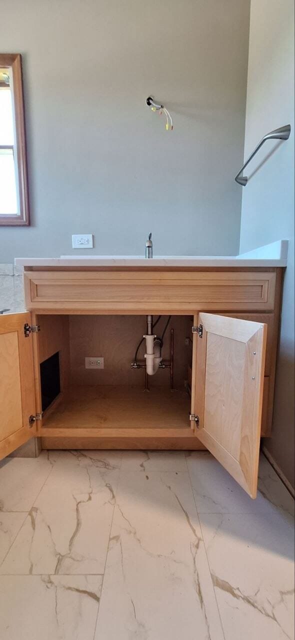 New bathroom vanity and faucet installed with the cabinet open to show the plumbing