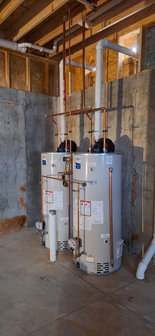 Two new tank water heaters with copper piping installed in an unfinished basement