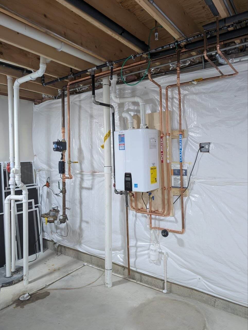 Tankless water heater installed in an unfinished basement with copper and PVC piping
