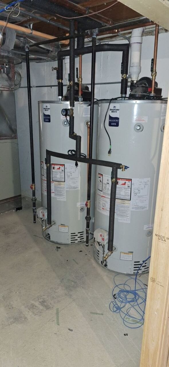 Two water heaters with black iron gas piping and shut-off valves